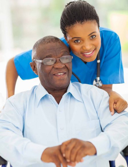 Smiling elderly man with a nurse in blue scrubs behind him.